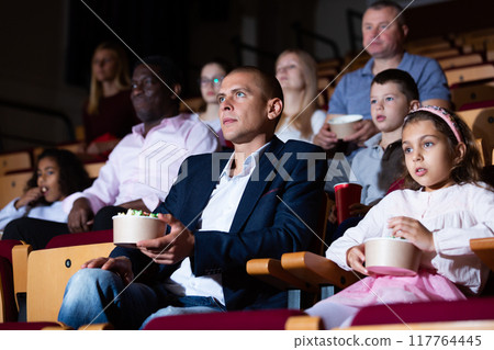 Father and tween daughter watching film together in cinema Father and tween daughter watching film together in cinema 117764445