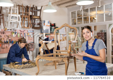 Cheerful young female furniture restorer showing his vintage furniture workshop Cheerful young female furniture restorer showing his vintage furniture workshop 117764510