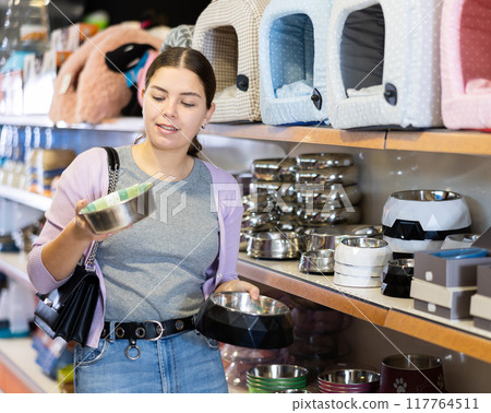 Young cheerful woman buying bowl for pets in pet store 117764511