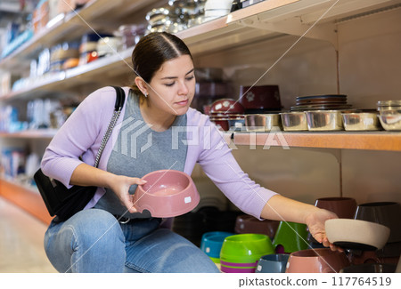 Young happy woman choosing bowl for pets in pet shop Young happy woman choosing bowl for pets in pet shop 117764519