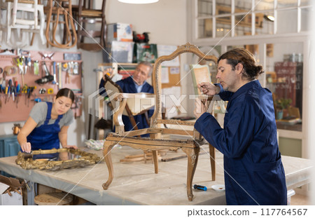 Male furniture maker working on vintage chair in workshop Male furniture maker working on vintage chair in workshop 117764567