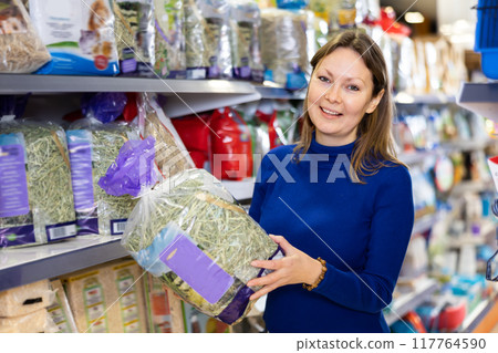 Happy woman picking out packed hay in pet shop 117764590