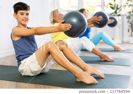 Family grandmother, mother and grandson perform fitness exercise sitting on floor with softball Family grandmother, mother and grandson perform fitness exercise sitting on floor with softball 117764594