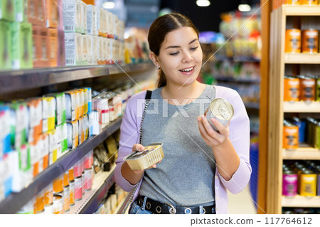 Young female customer picking out canned pet food in pet store Young female customer picking out canned pet food in pet store 117764612