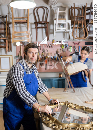 Male furniture maker diligently working on vintage mirror in workshop 117764670