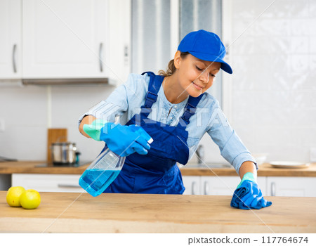 Skilled woman house cleaner sanitizing kitchen countertop 117764674