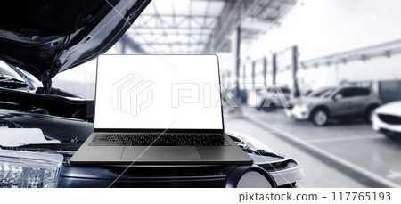 Grey laptop with blank white screen on the car engine compartment in the auto repair service garage Grey laptop with blank white screen on the car engine compartment in the auto repair service garage 117765193