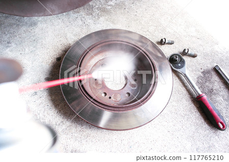 A mechanic cleans the inside of a car disc brake or drum brake with cleaning spray 117765210