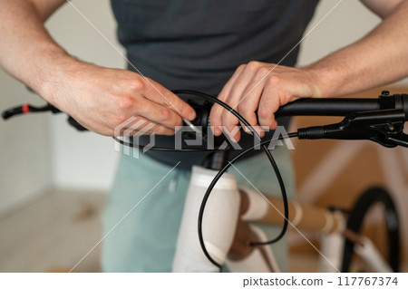 A man is inside working on assembling bike handlebars as part of his bicycle maintenance task 117767374