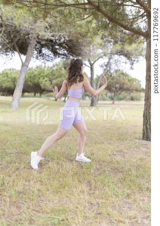A Woman Dressed in Purple Sportswear Is Seen Exercising Vigorously in a Beautiful Park Setting 117769692