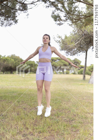 A Young Woman Happily Jumping in a Beautiful Park on a Bright and Sunny Day, Enjoying the Warm Weather A Young Woman Happily Jumping in a Beautiful Park on a Bright and Sunny Day, Enjoying the Warm Weather 117769768