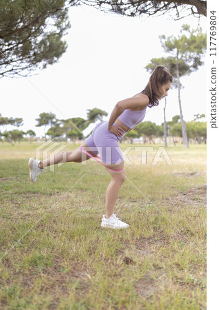 A Woman in the Park Is Performing Leg Exercises Using a Resistance Band to Strengthen and Tone Her Muscles A Woman in the Park Is Performing Leg Exercises Using a Resistance Band to Strengthen and Tone Her Muscles 117769804
