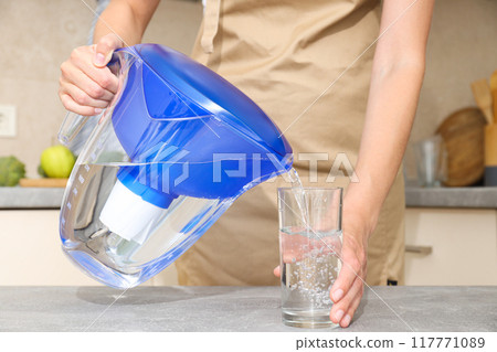 A water filter stands in the kitchen with a glass of water 117771089