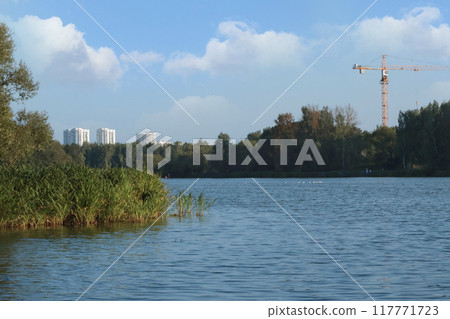 Water lake near city in summer with green plants. Nature and high-rise buildings, lifestyle. Ecology in Europe.  117771723
