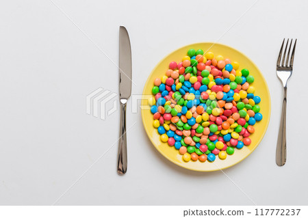 cutlery on table and sweet plate of candy. Health and obesity concept, top view on colored background cutlery on table and sweet plate of candy. Health and obesity concept, top view on colored background 117772237