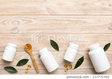 Omega-3 capsules lie in white bottle on a table with green leaves background. Fish oil tablets. Biologically active additives. omega 6, omega 9, vitamin A, E, D, vitamin D3 top view with copy space Omega-3 capsules lie in white bottle on a table with green leaves background. Fish oil tablets. Biologically active additives. omega 6, omega 9, vitamin A, E, D, vitamin D3 top view with copy space 117772302