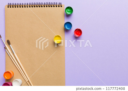 Album pages and paints, pencils, brush on a colored background. Top view with empty space. workplace for creativity. home teaching concept drawing Album pages and paints, pencils, brush on a colored background. Top view with empty space. workplace for creativity. home teaching concept drawing 117772408