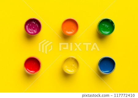 jars with gouache of different colors on Colored background. hobby painting. Top view with empty space. workplace for creativity. home teaching concept drawing 117772410