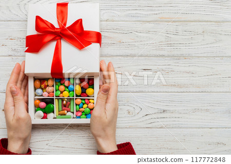 Female hands with delicious candies in box on color background Female hands with delicious candies in box on color background 117772848