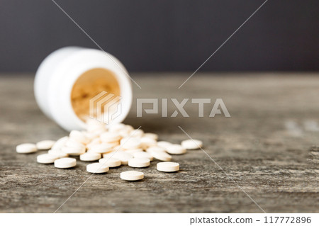 Medicine bottle and white pills spilled on a light background. Medicines and prescription pills flat lay background. White medical pills and tablets spilling out of a drug bottle Medicine bottle and white pills spilled on a light background. Medicines and prescription pills flat lay background. White medical pills and tablets spilling out of a drug bottle 117772896