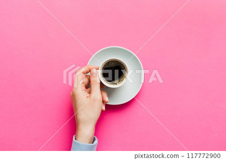 Minimalistic style woman hand holding a cup of coffee on Colored background. Flat lay, top view cappuccino cup. Empty place for text, copy space. Coffee addiction. Top view, flat lay 117772900