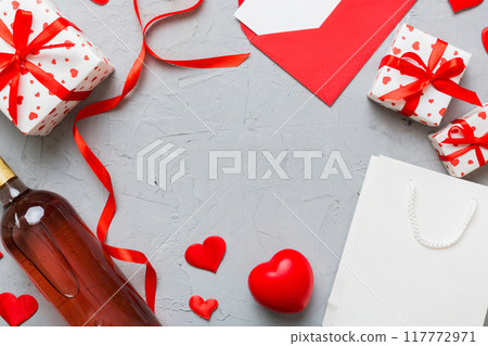 top view photo of st valentine day decor shopping, bag, wine, bottle, envelope, gift, box, candy and red heart on colored background with empty space. Frame background 117772971