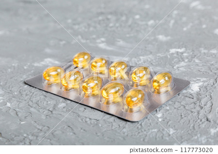 Blister package with fish oil capsules on color background. Medicine pills on a light background. Medicines and prescription pills flat lay background. Yellow medical tablets in blister Blister package with fish oil capsules on color background. Medicine pills on a light background. Medicines and prescription pills flat lay background. Yellow medical tablets in blister 117773020