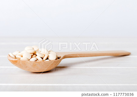 Heap of white pills on colored background. Tablets scattered on a table. Pile of red soft gelatin capsule. Vitamins and dietary supplements concept Heap of white pills on colored background. Tablets scattered on a table. Pile of red soft gelatin capsule. Vitamins and dietary supplements concept 117773036