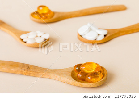 Vitamin capsules in a spoon on a colored background. Pills served as a healthy meal. Red soft gel vitamin supplement capsules on spoon Vitamin capsules in a spoon on a colored background. Pills served as a healthy meal. Red soft gel vitamin supplement capsules on spoon 117773039
