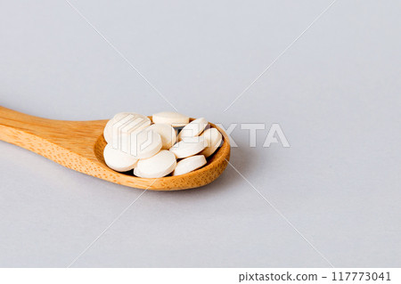 Heap of white pills on colored background. Tablets scattered on a table. Pile of red soft gelatin capsule. Vitamins and dietary supplements concept Heap of white pills on colored background. Tablets scattered on a table. Pile of red soft gelatin capsule. Vitamins and dietary supplements concept 117773041