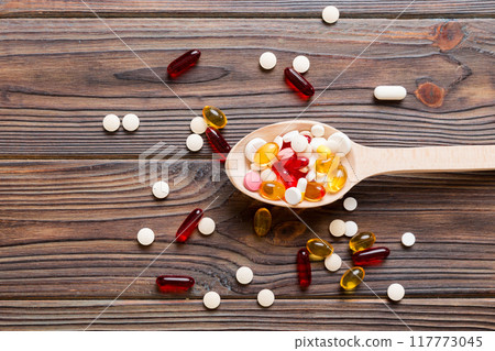Vitamin capsules in a spoon on a colored background. Pills served as a healthy meal. Red soft gel vitamin supplement capsules on spoon Vitamin capsules in a spoon on a colored background. Pills served as a healthy meal. Red soft gel vitamin supplement capsules on spoon 117773045
