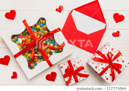 Red envelope with candy and gift box and Valentines hearts on colored background. Flat lay, top view. Romantic love letter for Holiday concept 117773064