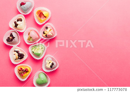 chocolate sweets in the form of a heart with fruits and nuts on a colored background. top view with space for text, holiday concept chocolate sweets in the form of a heart with fruits and nuts on a colored background. top view with space for text, holiday concept 117773078
