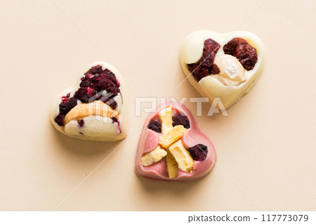 chocolate sweets in the form of a heart with fruits and nuts on a colored background. top view with space for text, holiday concept chocolate sweets in the form of a heart with fruits and nuts on a colored background. top view with space for text, holiday concept 117773079