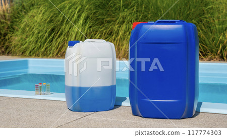 Two large plastic containers for pool chemicals are placed by the poolside, with a water testing kit visible in the background. Two large plastic containers for pool chemicals are placed by the poolside, with a water testing kit visible in the background. 117774303