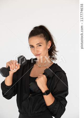 Young girl posing with dumbbells for power training, indoors. athlete wearing black leggings and shirt Young girl posing with dumbbells for power training, indoors. athlete wearing black leggings and shirt 117774638