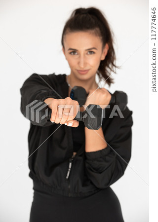 Young girl posing with dumbbells for power training, indoors. athlete wearing black leggings and shirt Young girl posing with dumbbells for power training, indoors. athlete wearing black leggings and shirt 117774646