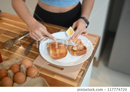 Above view of young woman making delicious bread, spreading butter on bread with a cutlery knife 117774720