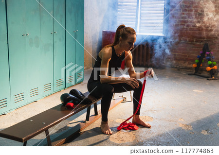 Women self defense girl power. Woman fighter preparing for fight wrapping hands with red boxing wraps sports protective bandages. Strong girl ready for fight active exercise sparring workout training 117774863