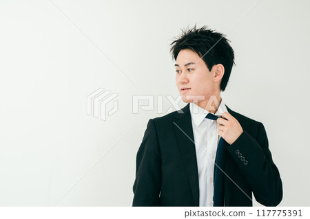 A man in his 20s with a tired expression loosening his tie 117775391