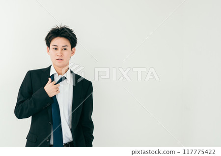 A man in his 20s with a tired expression loosening his tie A man in his 20s with a tired expression loosening his tie 117775422