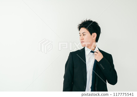 A man in his 20s looking to the side while loosening his tie 117775541