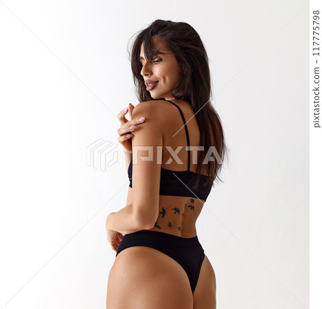 Confident woman poses in black lingerie, shows her side profile with flowing hair, and subtle smile against a white background. 117775798