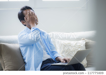 Middle-aged man using a laptop in the living room Middle-aged man using a laptop in the living room 117775809
