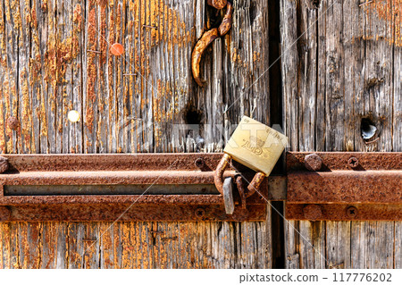 Rusty padlock mounted on an old, weathered wooden door, close up Rusty padlock mounted on an old, weathered wooden door, close up 117776202