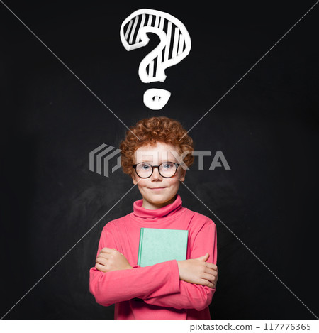 Cute kid school student boy holding book against blackboard background with question mark. Cute kid school student boy holding book against blackboard background with question mark. 117776365