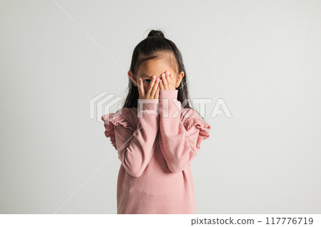 Asian portrait young kid girl in depressed bad mood covering face with hands and peering out with one eye between fingers studio isolated on white background, kindergarten child surprised and shocked Asian portrait young kid girl in depressed bad mood covering face with hands and peering out with one eye between fingers studio isolated on white background, kindergarten child surprised and shocked 117776719