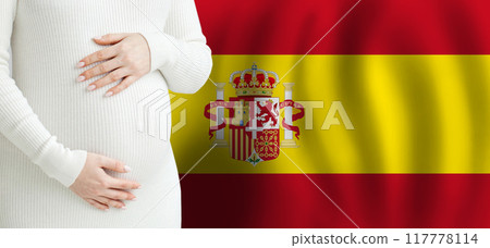Pregnant woman belly against Spanish flag background. Demographics and pregnancy in Spain concept 117778114