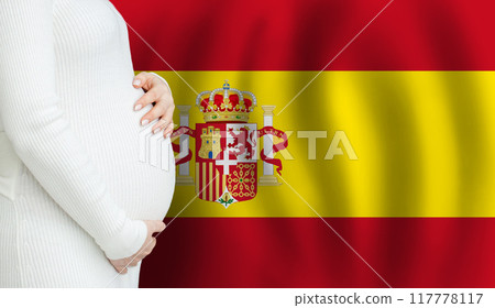 Pregnant woman belly against Spanish flag background. Demographics and pregnancy in Spain concept 117778117