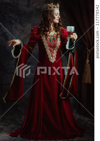 Full length portrait of medieval queen in red dress with goblet 117778542
